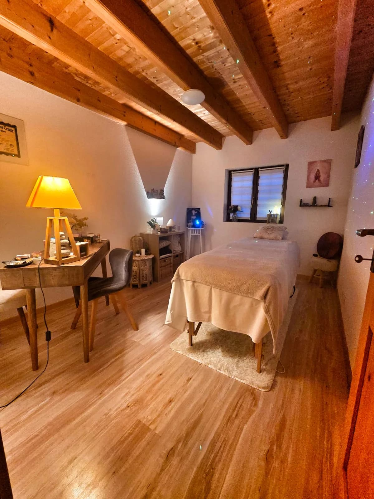 Vue d'ensemble de la salle de soin avec table de massage, bureau et plafond en poutres de bois